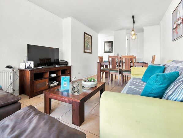 Een woonkamer met een televisie, houten meubels en een eethoek met stoelen en een tafel.
