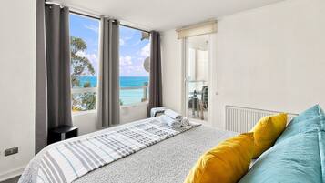Quarto com cama, vista para o mar e janela com cortinas.