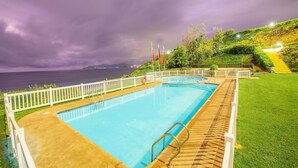 A swimming pool with a white fence, a grassy area, and a view of the sea under a cloudy sky. - Oceana Suites Costa Quilen (Puchuncavi)