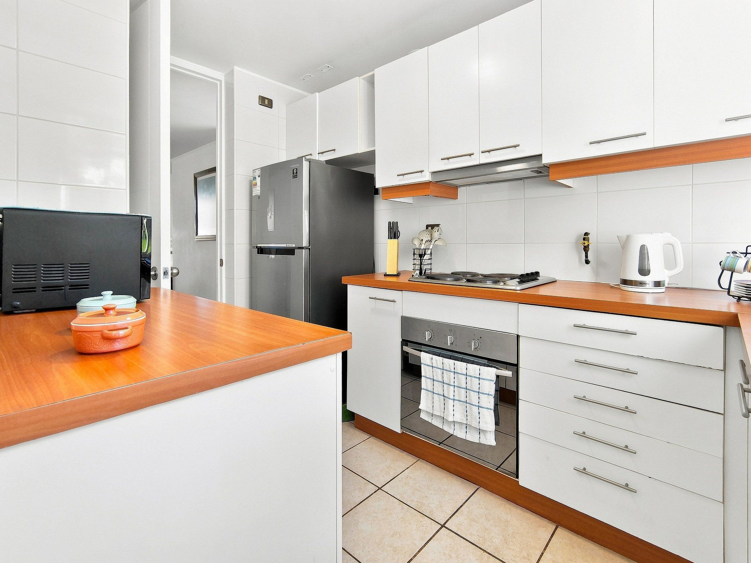 A modern kitchen with white cabinets, a wooden countertop, a built-in oven, and a black refrigerator.