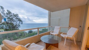 A balcony with a glass table and white chairs, overlooking a coastal view. - Oceana Suites Costa Quilen (Puchuncavi)