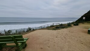 A sandy beach with a green bench, a fence, and a sign indicating no swimming. - Oceana Suites Costa Quilen (Puchuncavi)