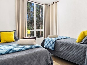 Een slaapkamer met twee bedden, een nachtkastje met een lamp en een raam met gordijnen.