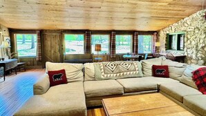 Ein gemütliches Wohnzimmer mit Holzbalkendecke, Steinwand und großen Fenstern.