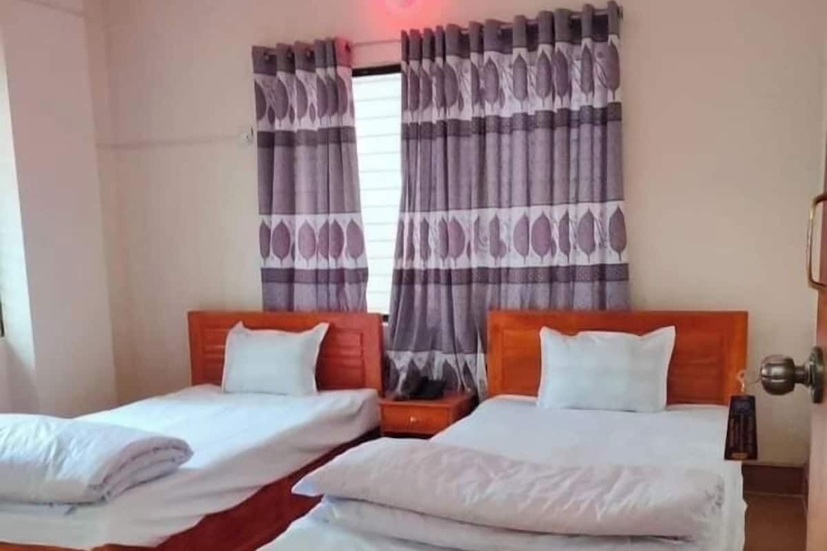 A hotel room with two wooden beds, a nightstand, and a window with patterned curtains.