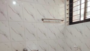 A bathroom with white marble tiles, a toilet, a sink, a red bucket, and a window with bars. - Hotel Stay Inn Dhaka (Dhaka)