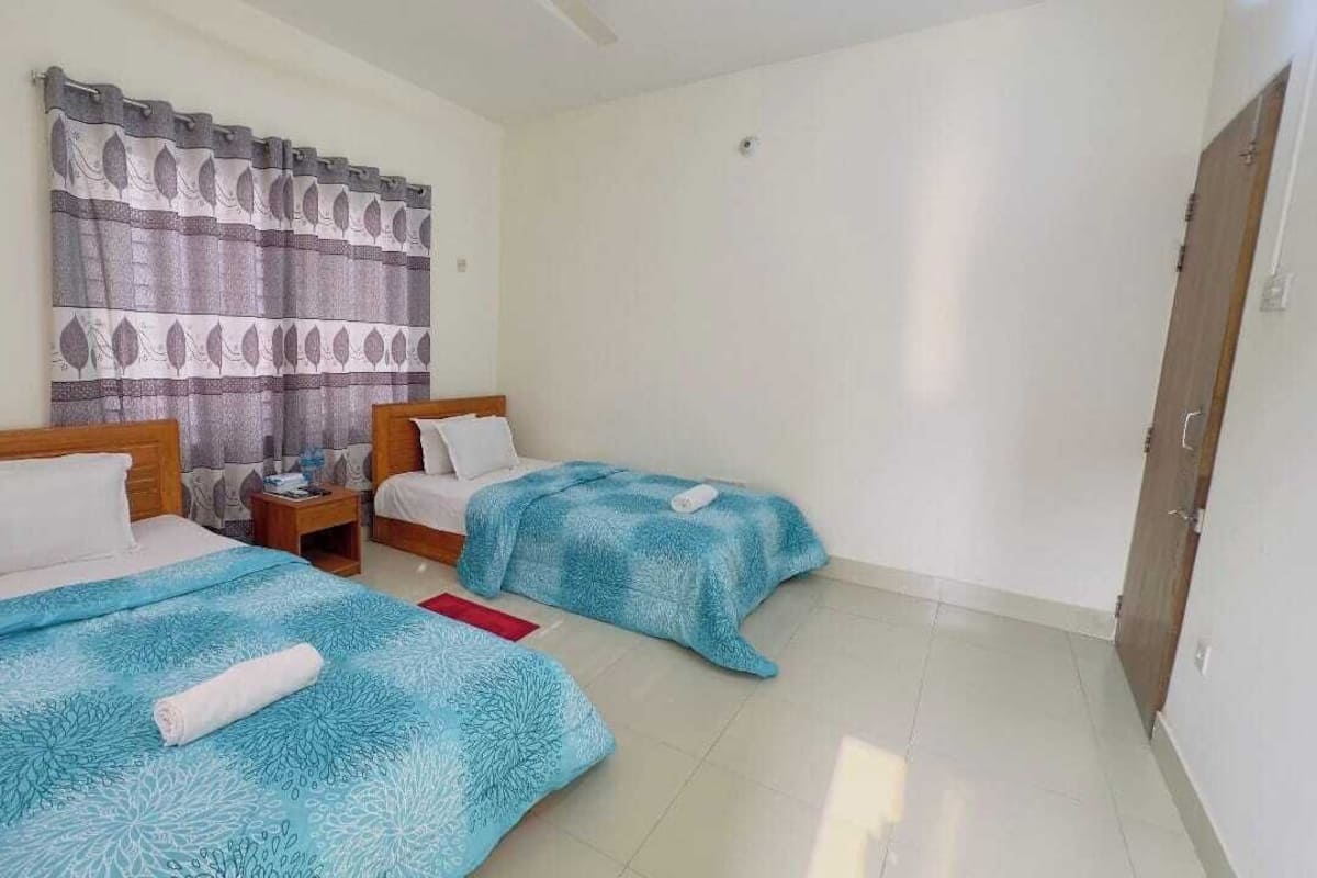 A hotel room with two beds, a wooden headboard, a nightstand, and a curtain with a leaf pattern.