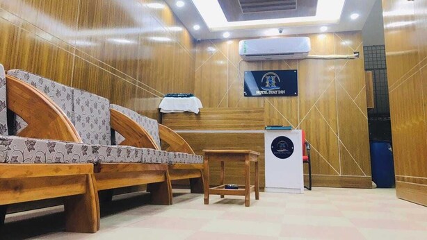 A hotel room with wooden paneling, a bed with patterned bedding, a small table, an air conditioning unit, and a sign with the hotel's name. - Hotel Stay Inn Dhaka (Dhaka)