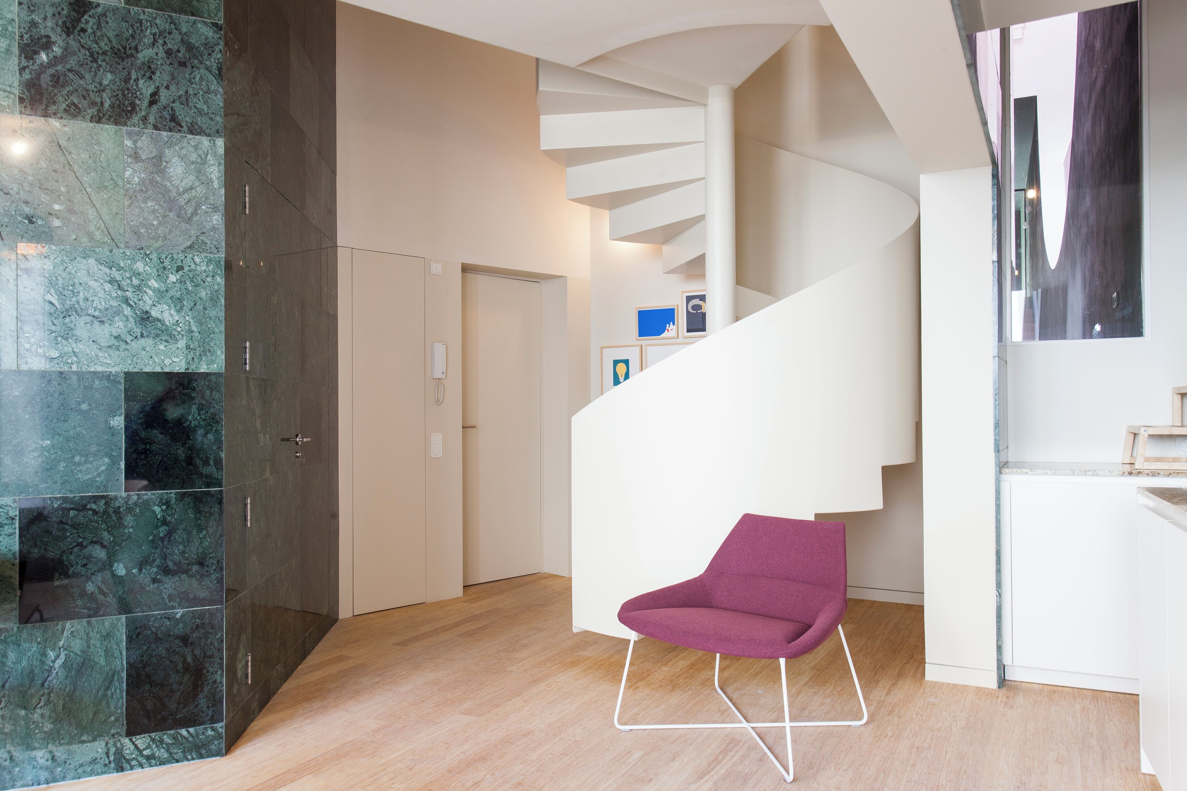 Un intérieur moderne avec un escalier en colimaçon, un fauteuil violet et un mur en marbre.