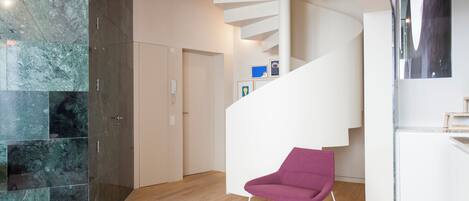 Un intérieur moderne avec un escalier en colimaçon, un fauteuil violet et un mur en marbre.