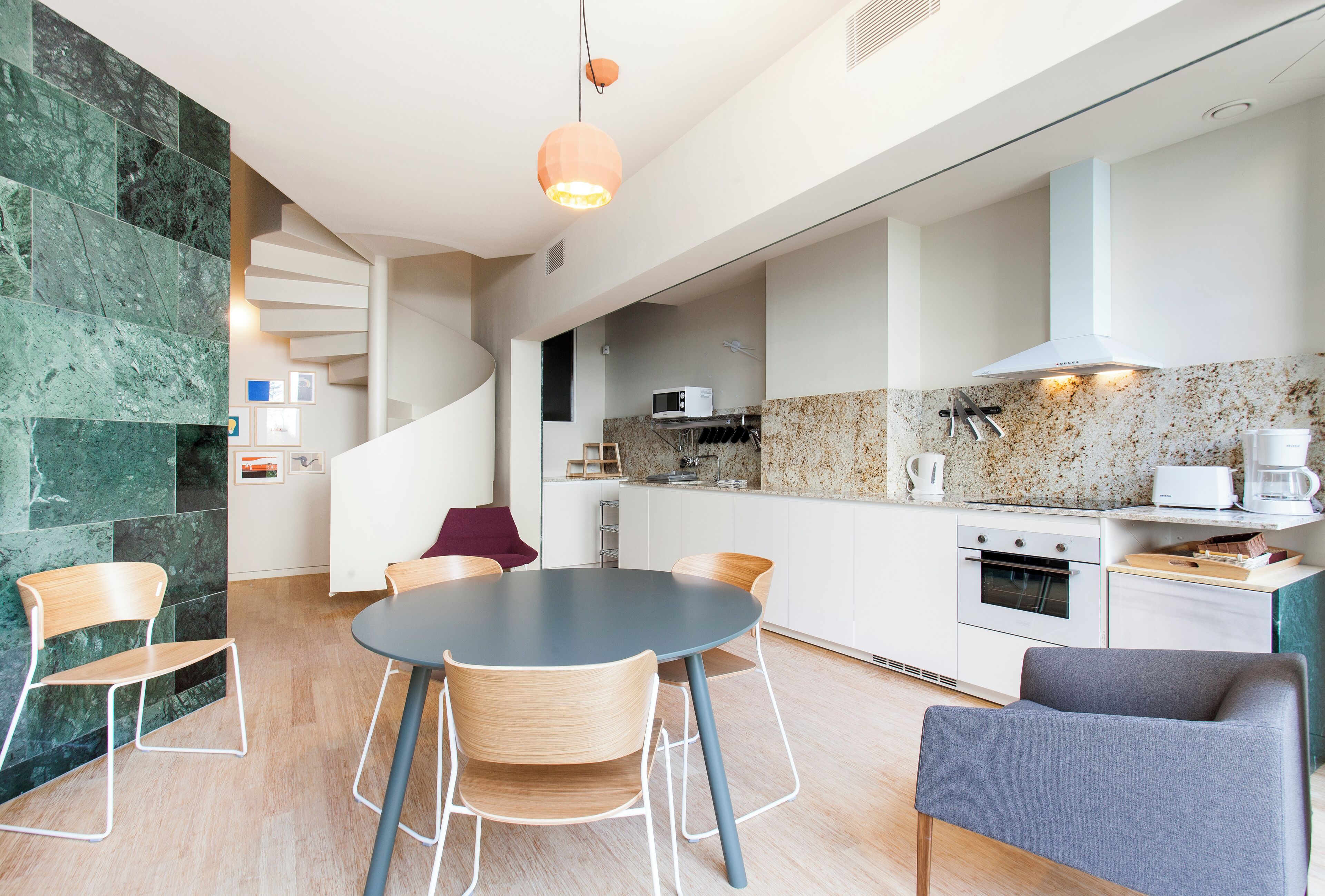A modern kitchen with a dining area, featuring a spiral staircase, granite countertops, and contemporary appliances.