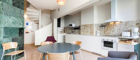 A modern kitchen with a dining area, featuring a spiral staircase, granite countertops, and contemporary appliances.