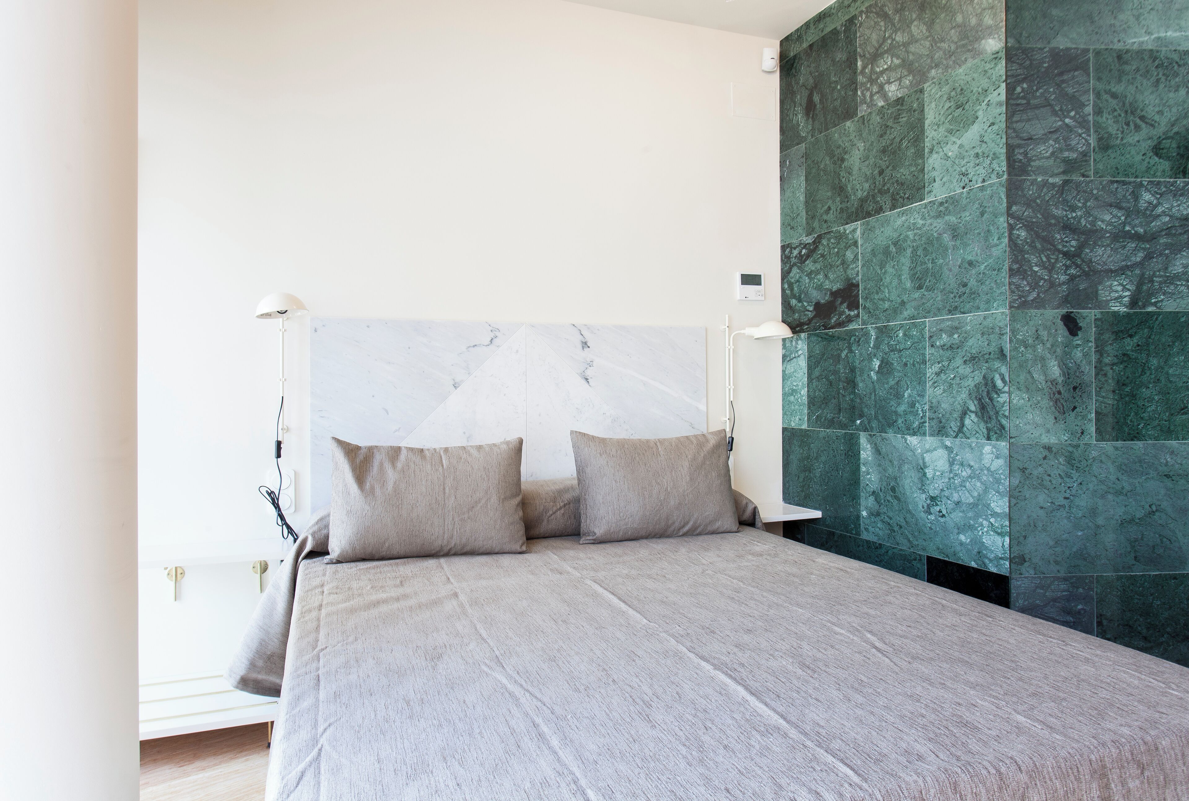 Een moderne slaapkamer met een marmeren hoofdbord, twee kussens, een bedlampje en een groene marmeren wand.