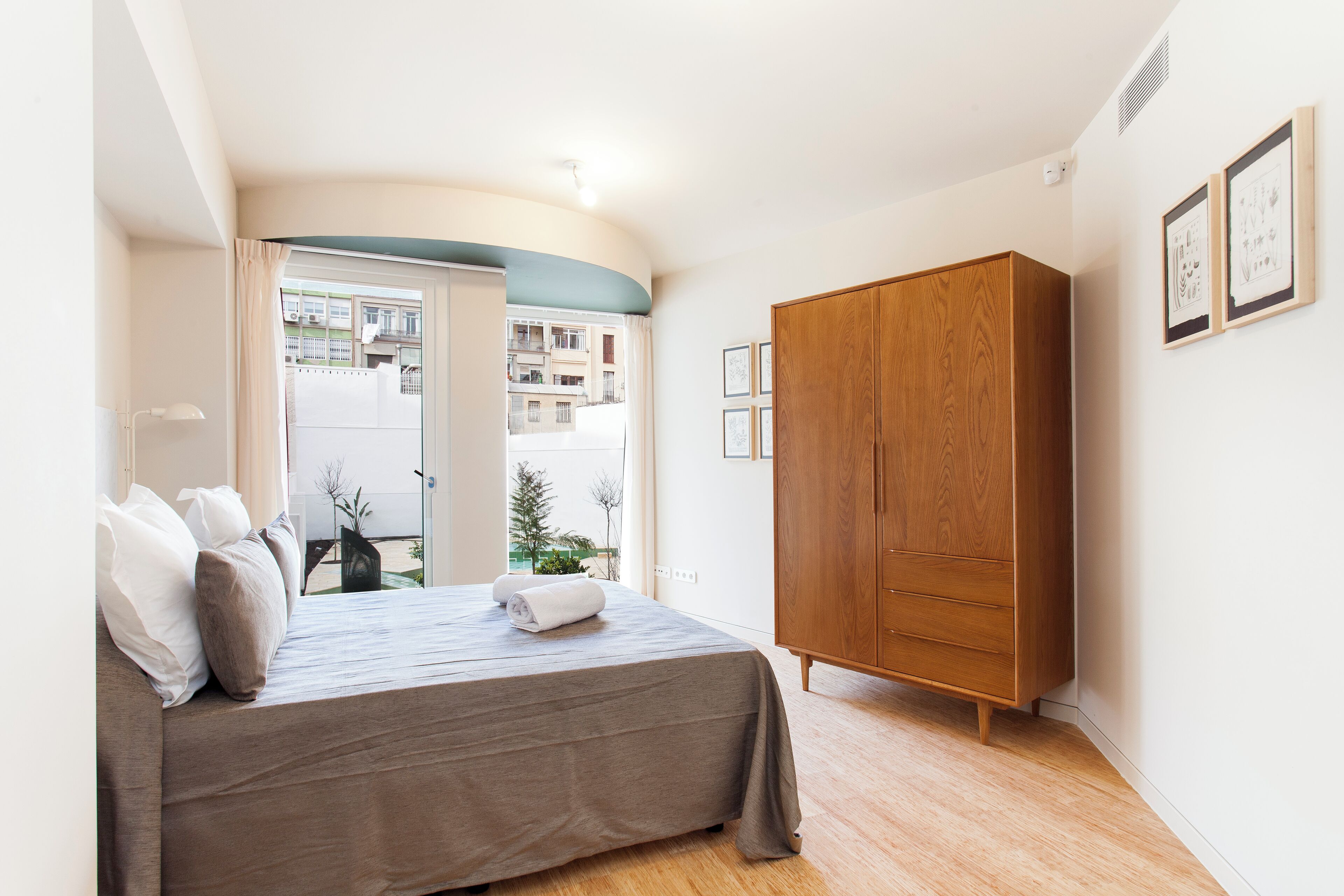 A bedroom with a bed, a wardrobe, and a window with a view of buildings.