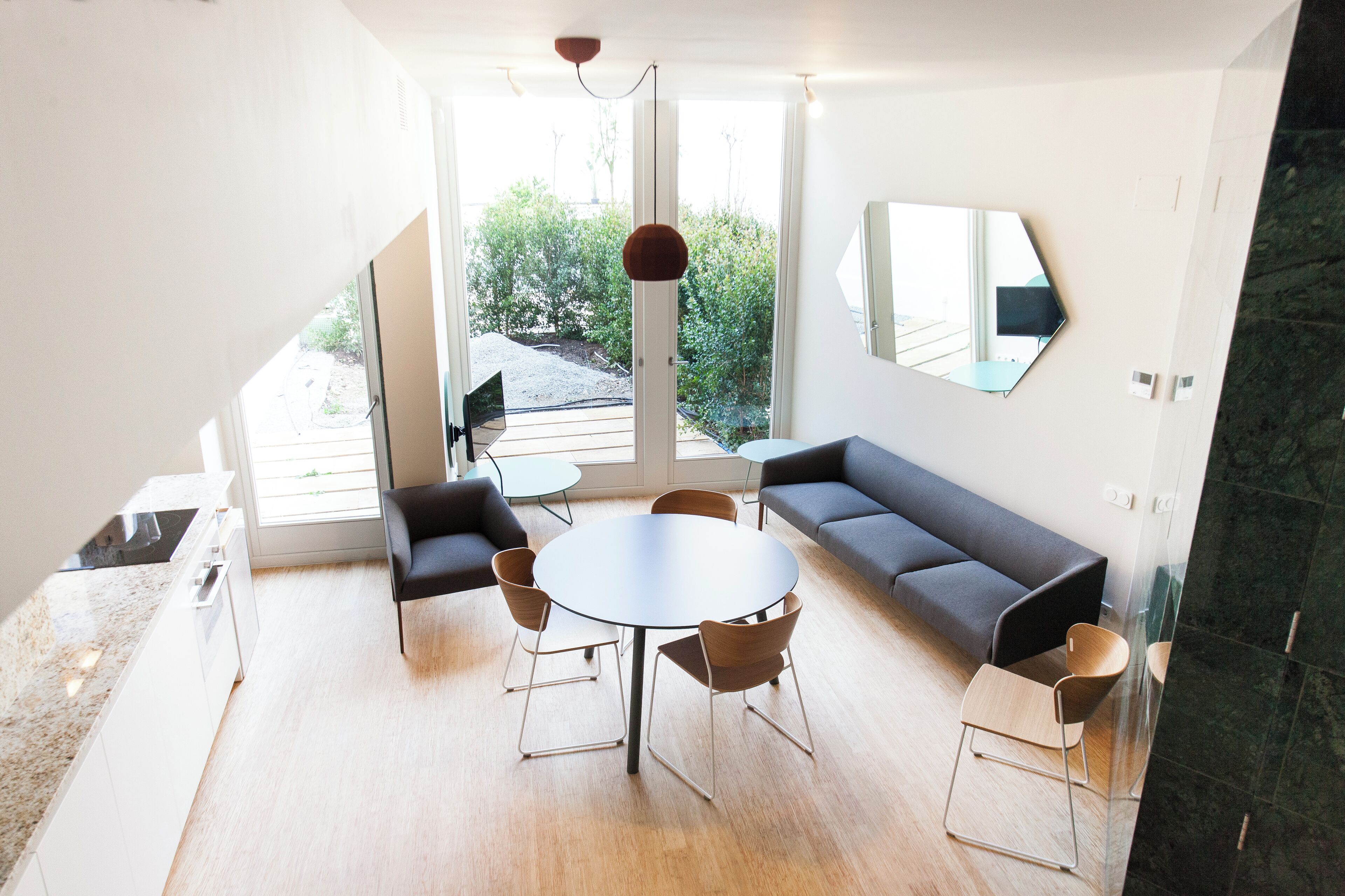 En moderne stue med et rundt bord, to sofaer og et stort vindue der giver udsigt til grønne omgivelser.