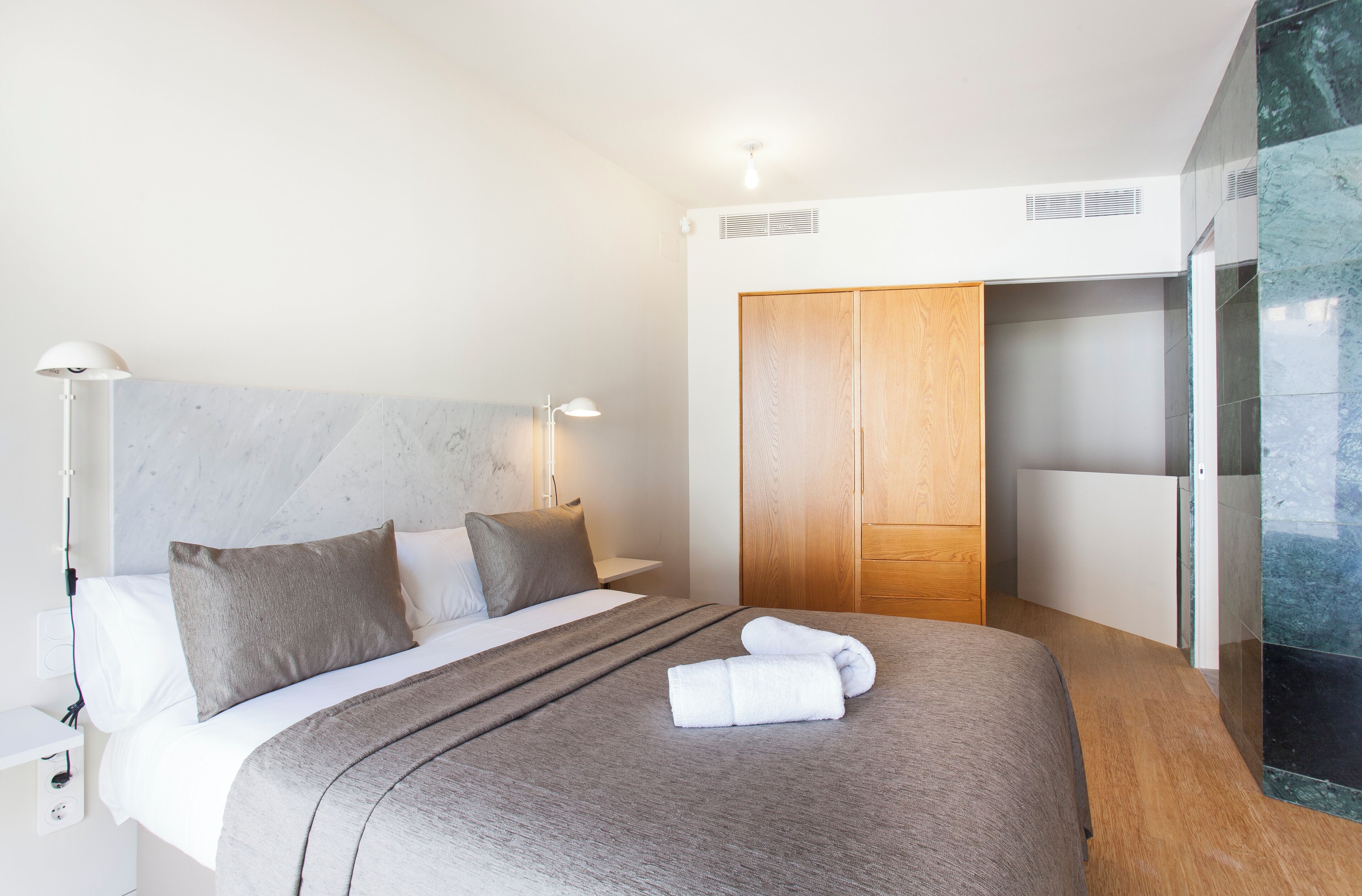 A modern hotel room with a large bed, a wooden wardrobe, and a glass partition.