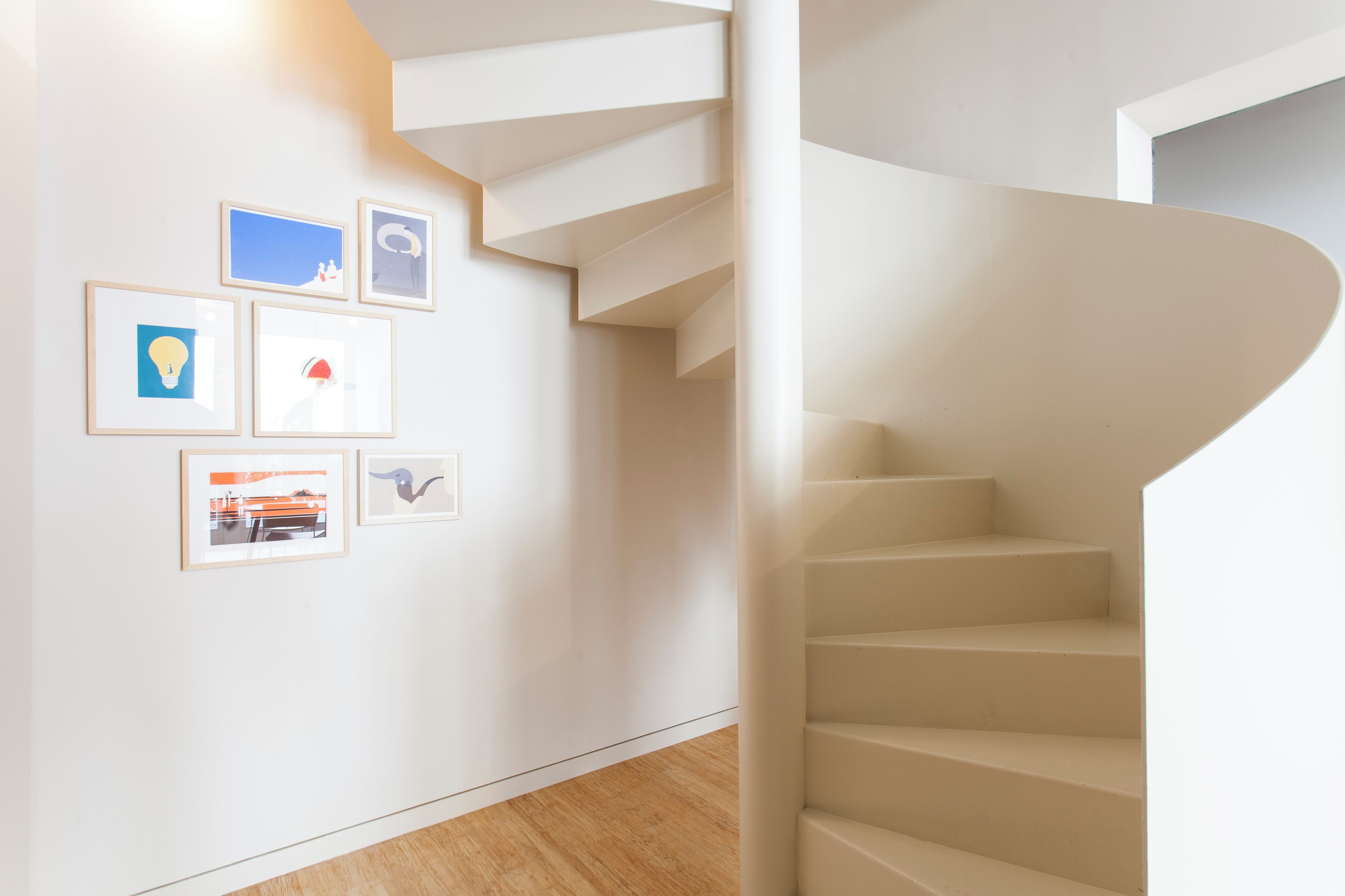 Un interior moderno con una escalera espiral, piso de madera y obras de arte enmarcadas en la pared.