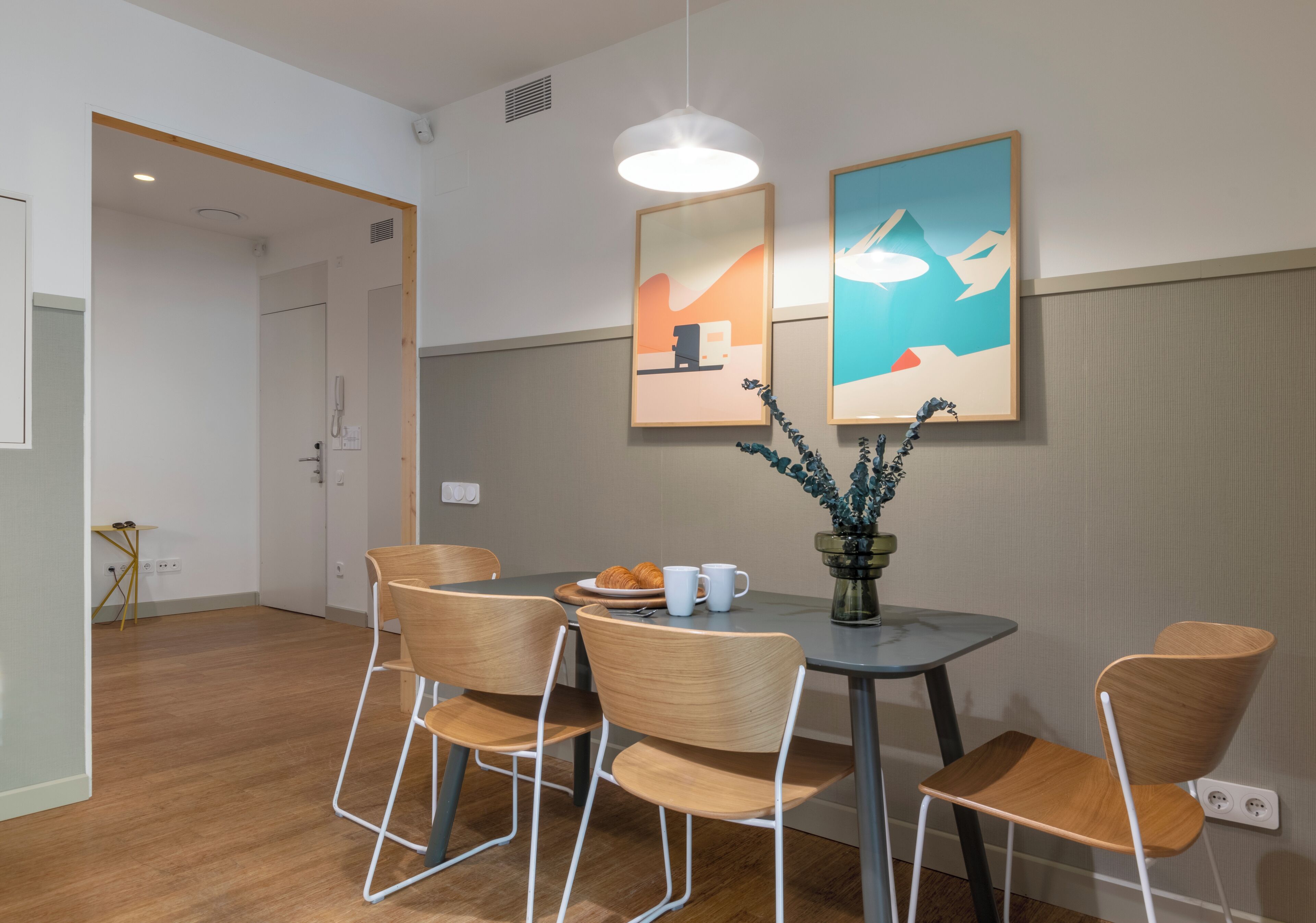 Un comedor moderno con una mesa redonda, cuatro sillas de madera y dos obras de arte enmarcadas en la pared.