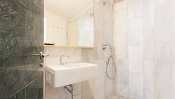 Een moderne badkamer met een wit wastafelmeubel, een douche en een wand betegeld met marmer.