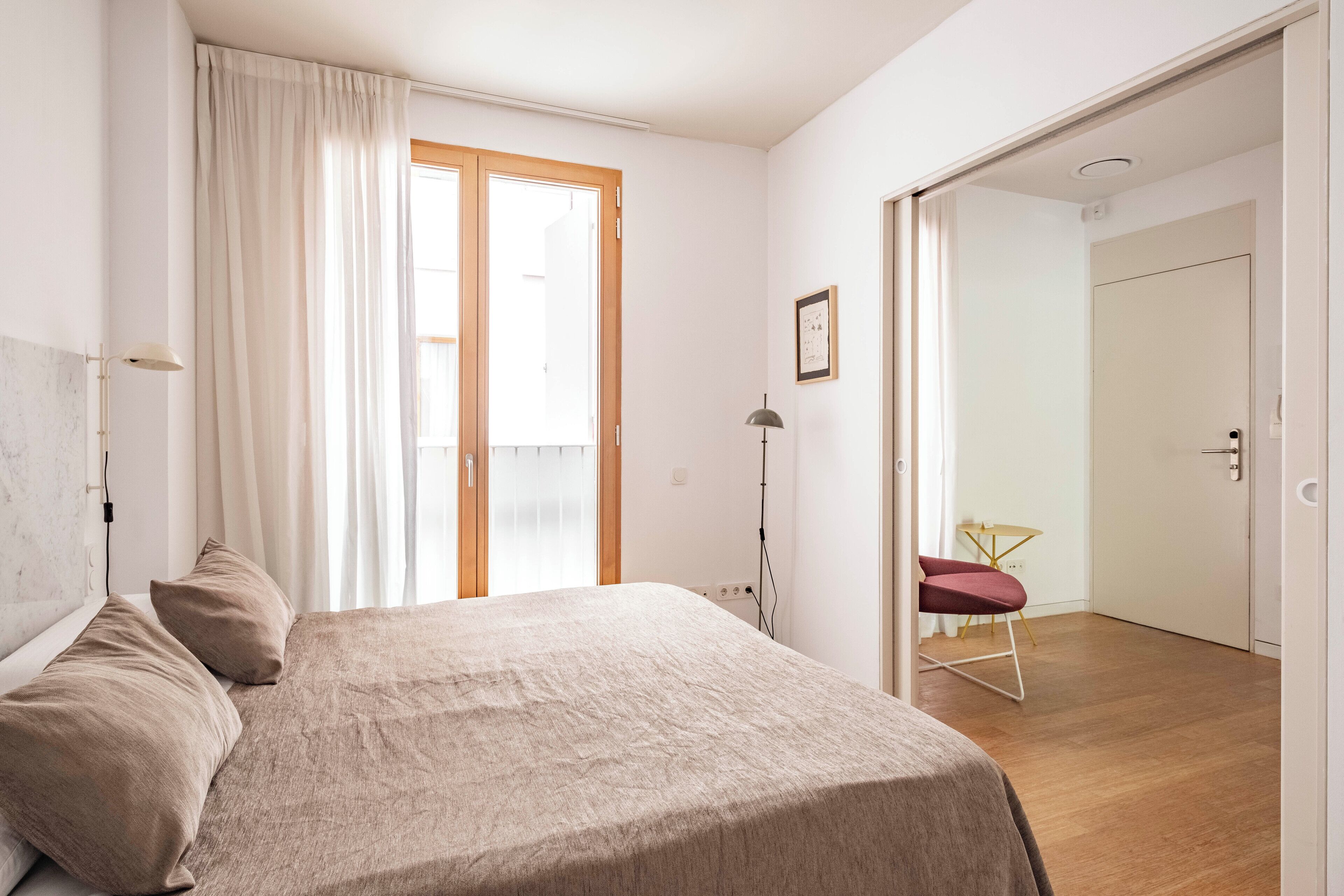 Ein Schlafzimmer mit Bett, Stuhl, Schreibtisch und einer Tür zu einem anderen Raum.