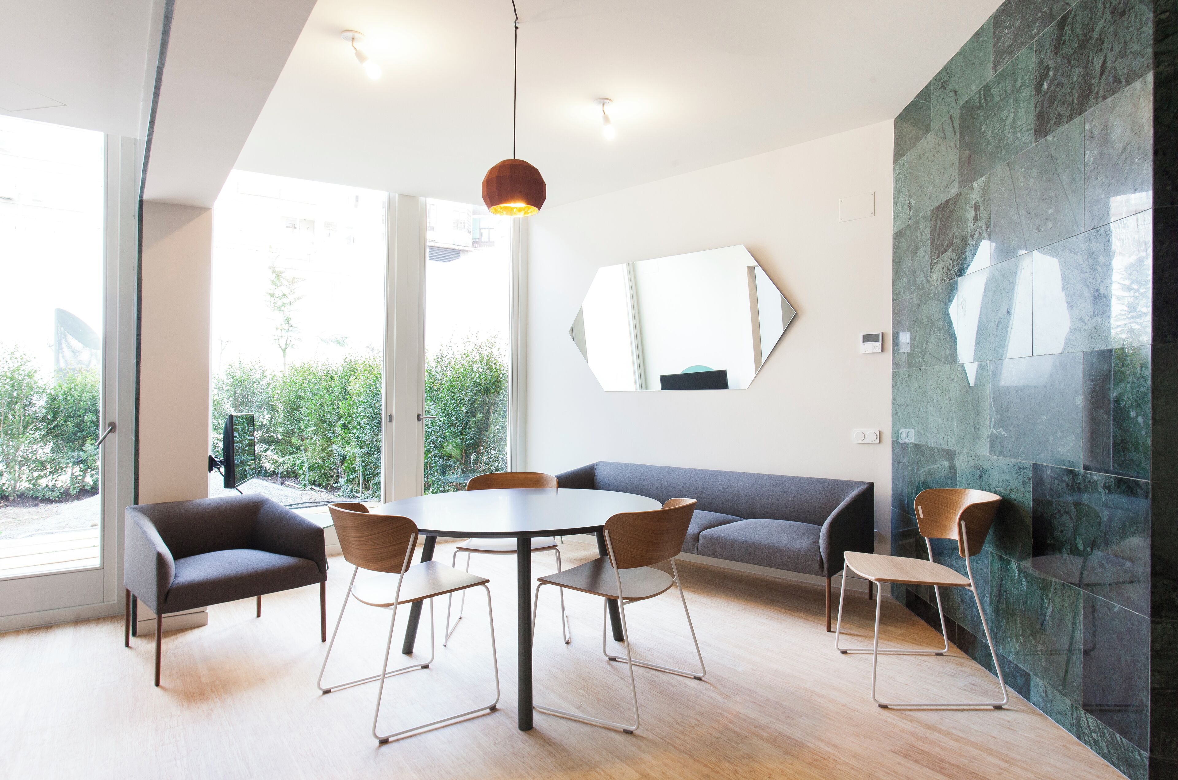 A modern dining area with a round table, six chairs, a sofa, and a large mirror on the wall.