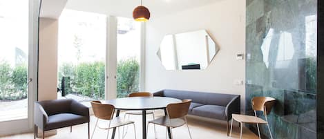 A modern dining area with a round table, six chairs, a sofa, and a large mirror on the wall.