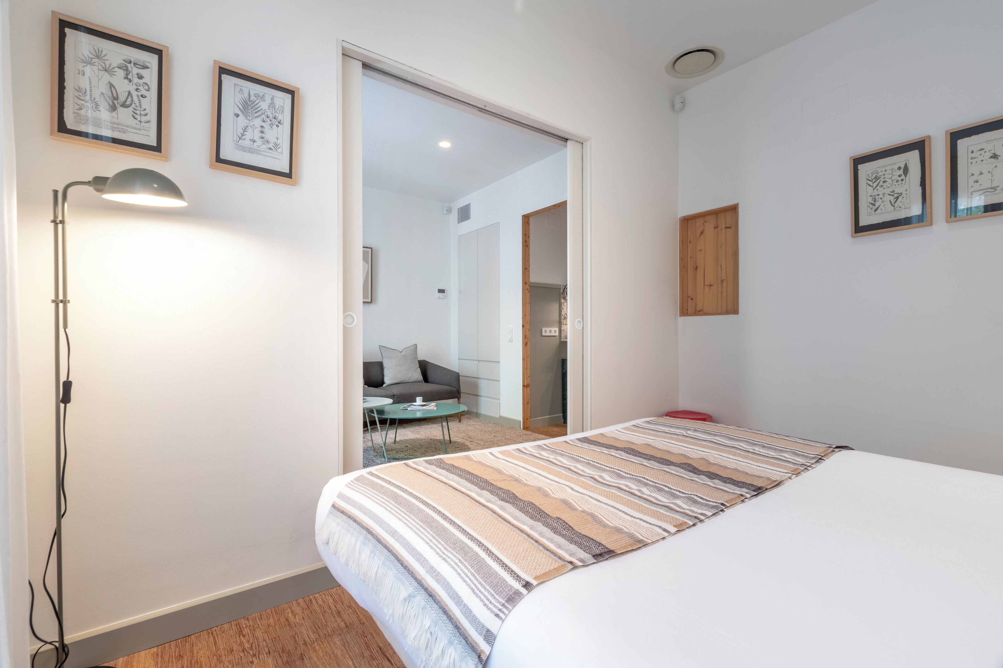 A bedroom with a bed, a lamp, and framed botanical prints on the wall.