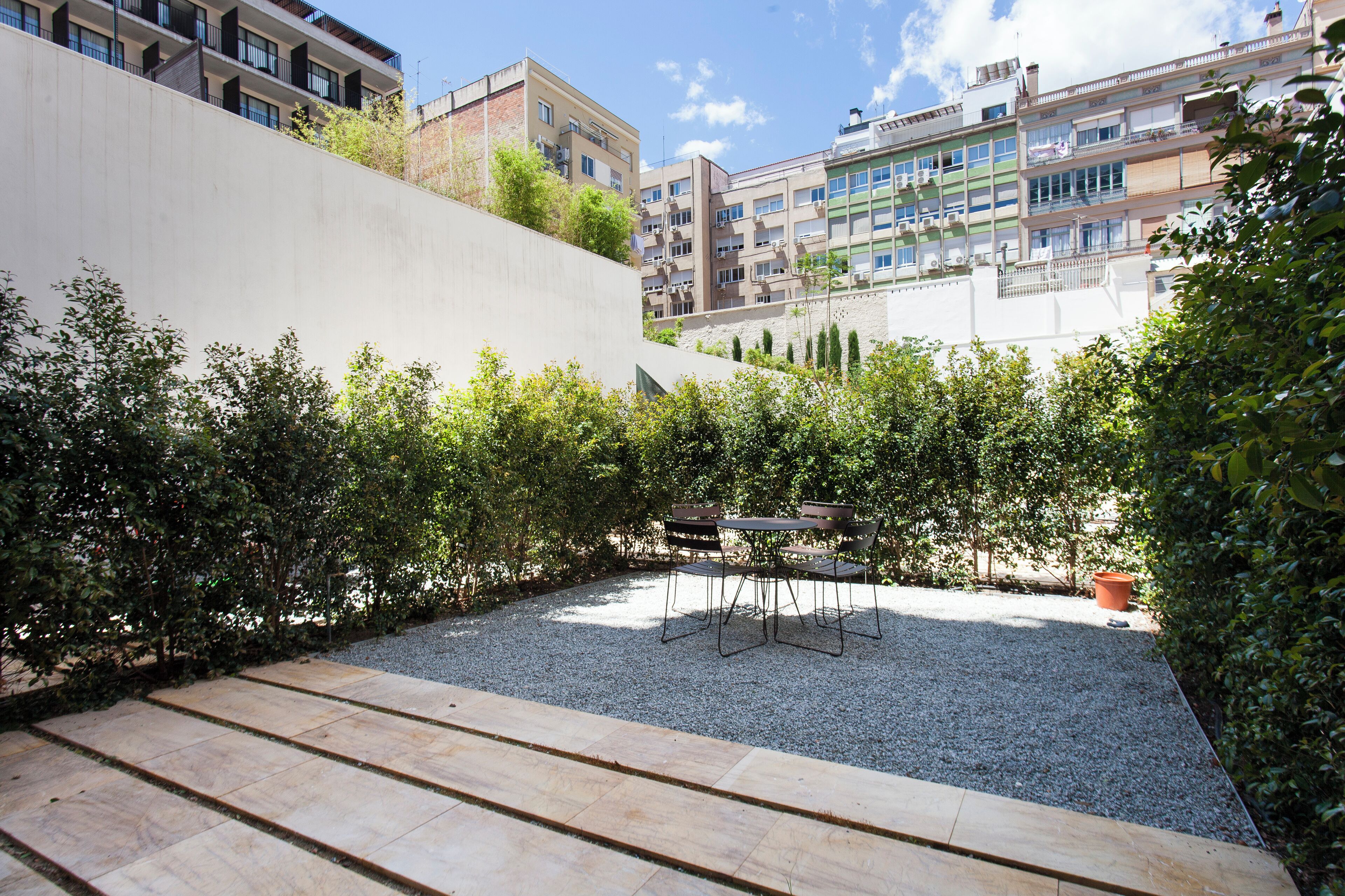 Un patio con zona de grava, una mesa y sillas, y una pared blanca.