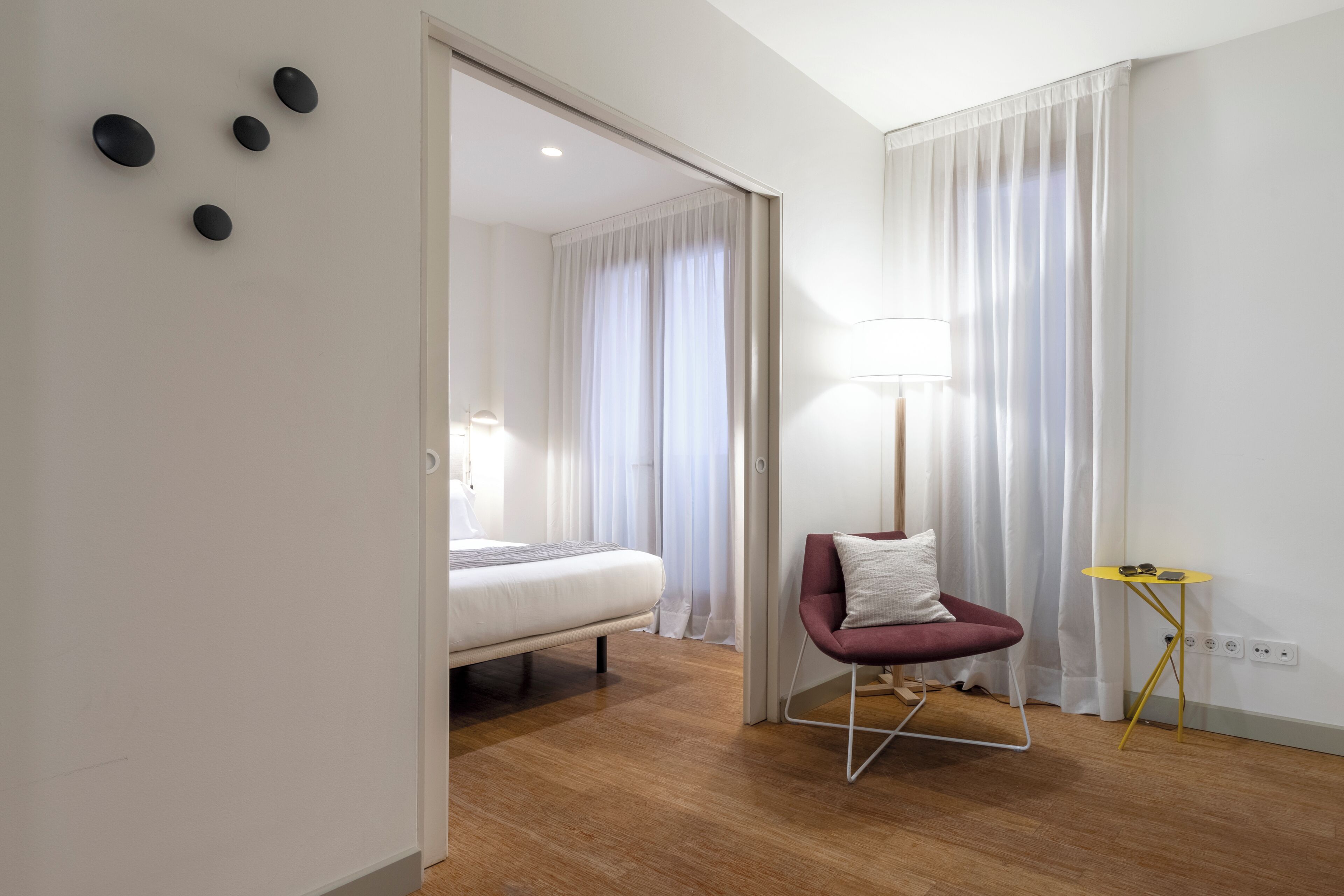 Una habitación de hotel moderna con una cama, una silla, una lámpara y una mesita.