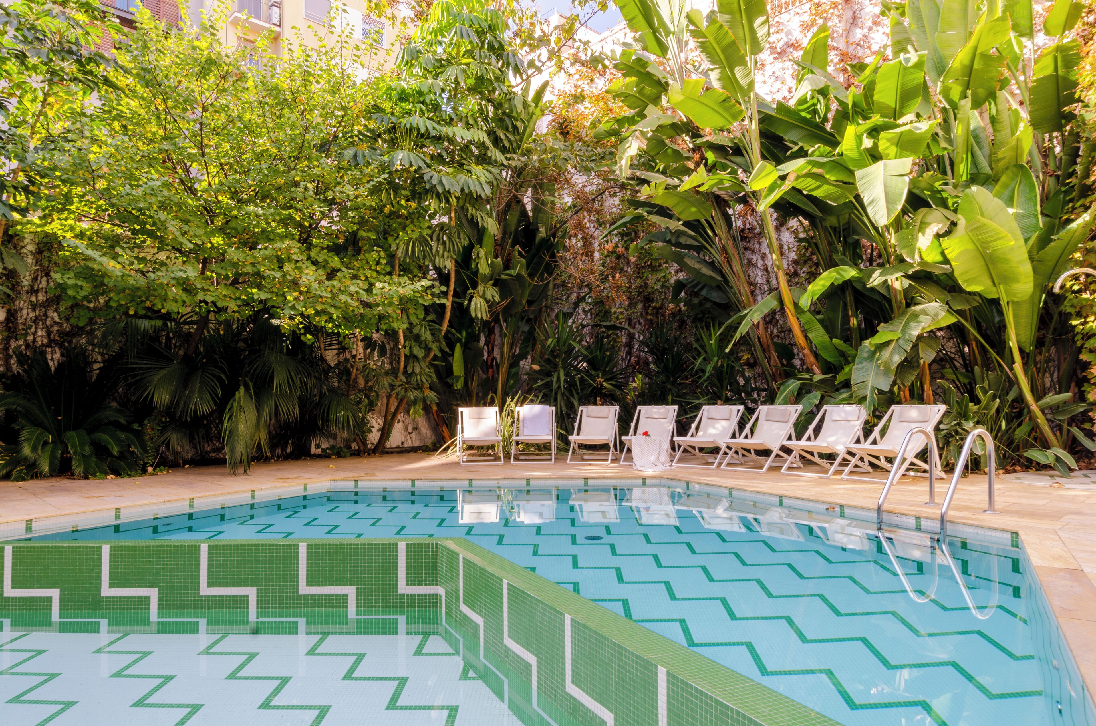 A swimming pool with a zigzag pattern, surrounded by lush greenery and white lounge chairs.