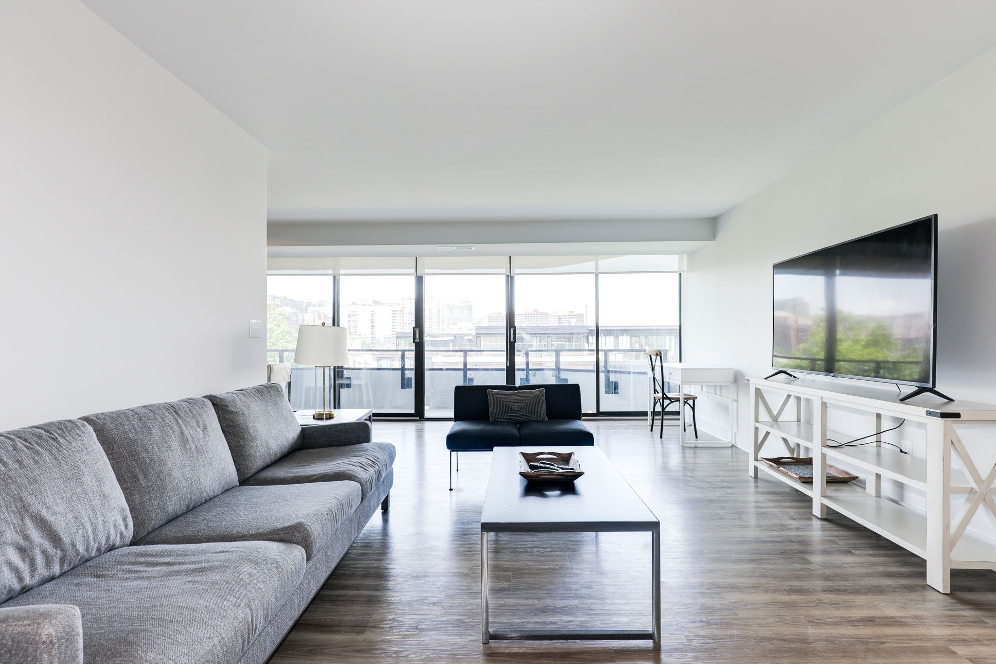 A modern living room with a grey sofa, a coffee table, and a TV on a white stand.