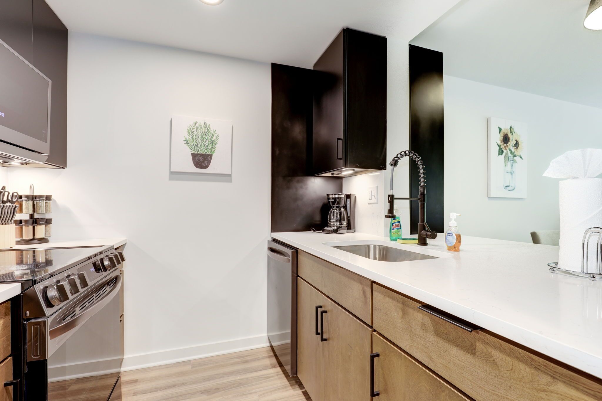 A modern kitchen with a stainless steel stove, wooden cabinets, a white countertop, and a sink.
