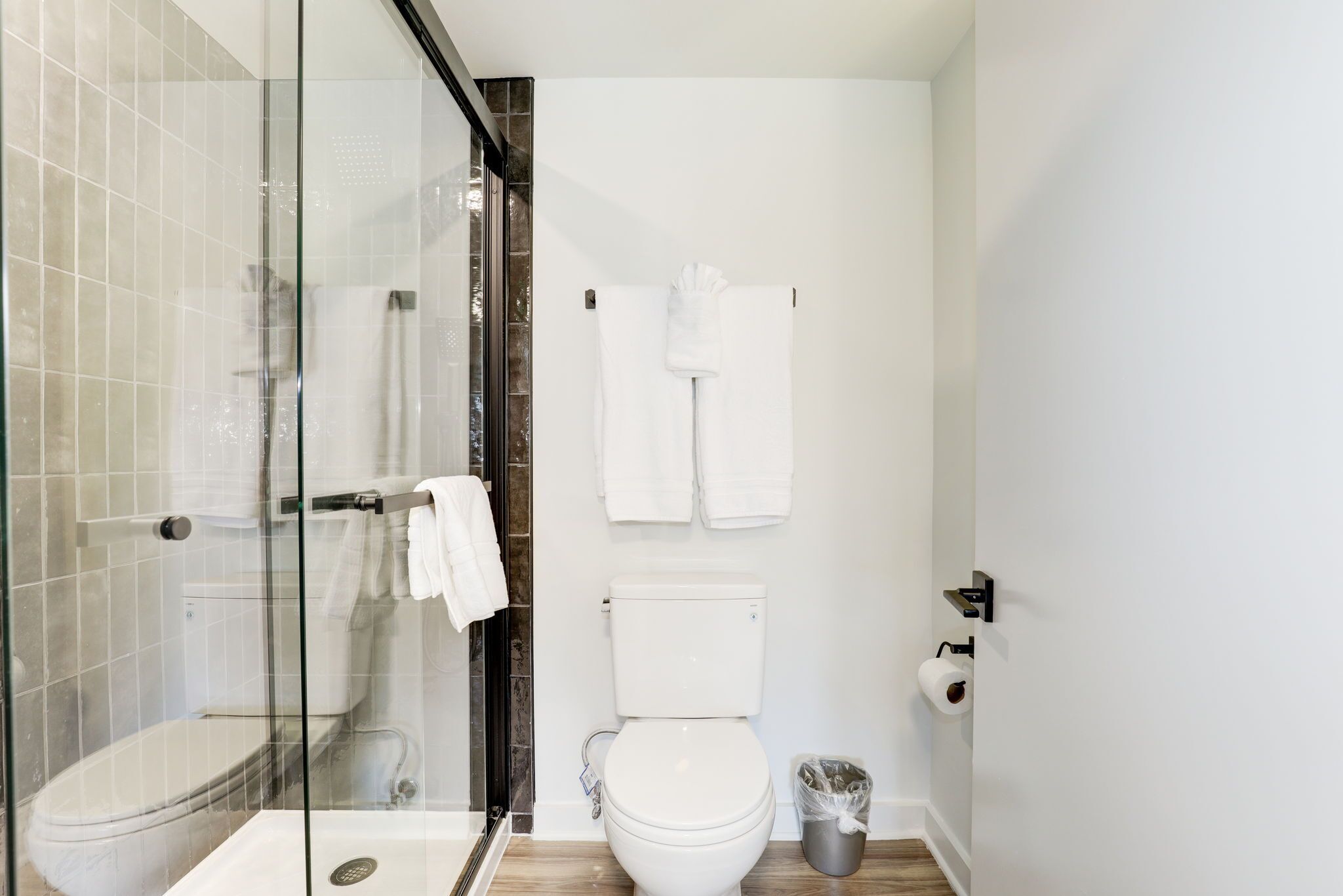 A modern bathroom with a glass-enclosed shower, a white toilet, and two towels hanging on the wall.