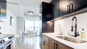 A modern kitchen with dark cabinetry, a stainless steel sink, and a dining area with a table and chairs. - Premium A-Location Apartment (Arlington)