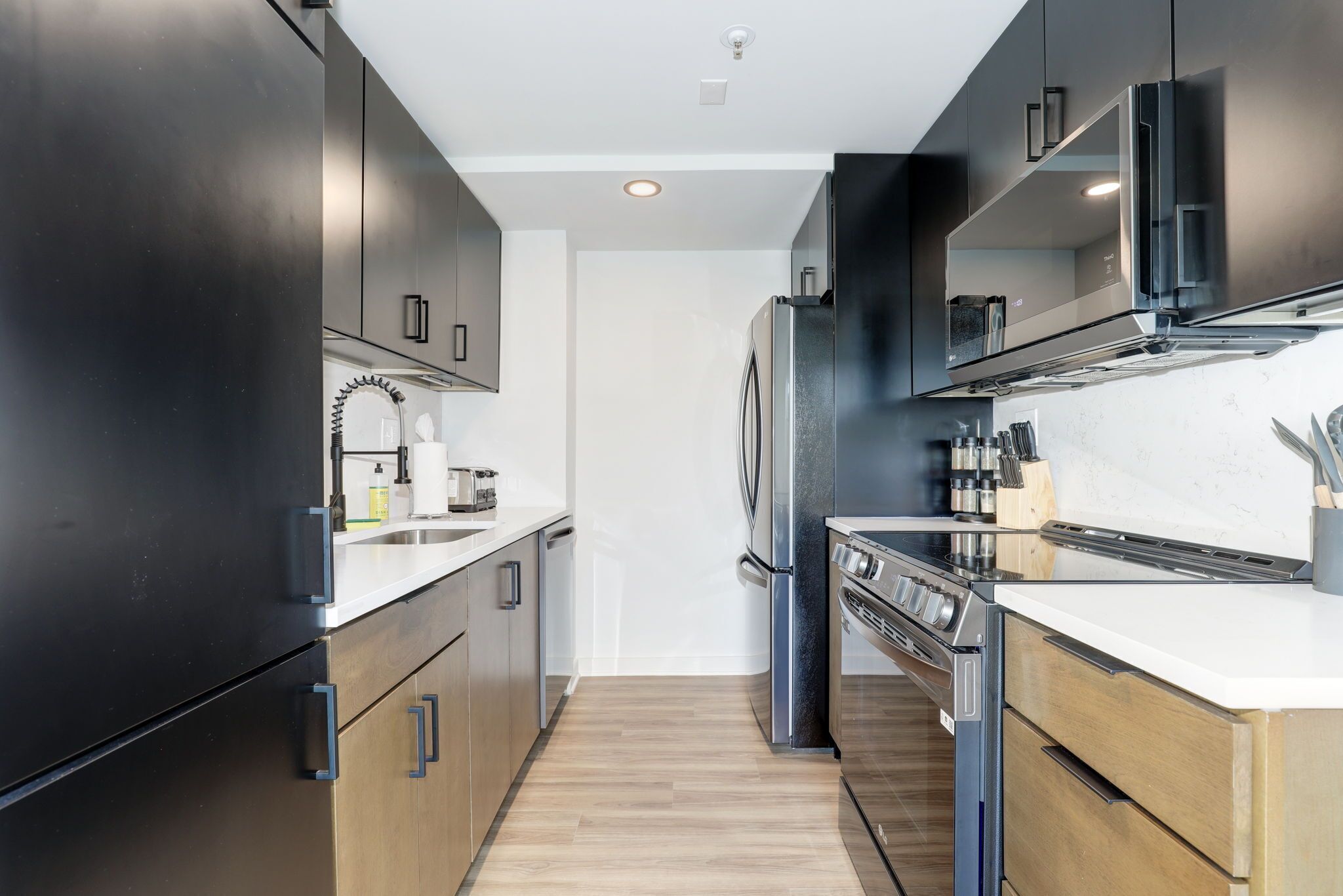 A modern kitchen with dark cabinets, stainless steel appliances, and a wooden floor.