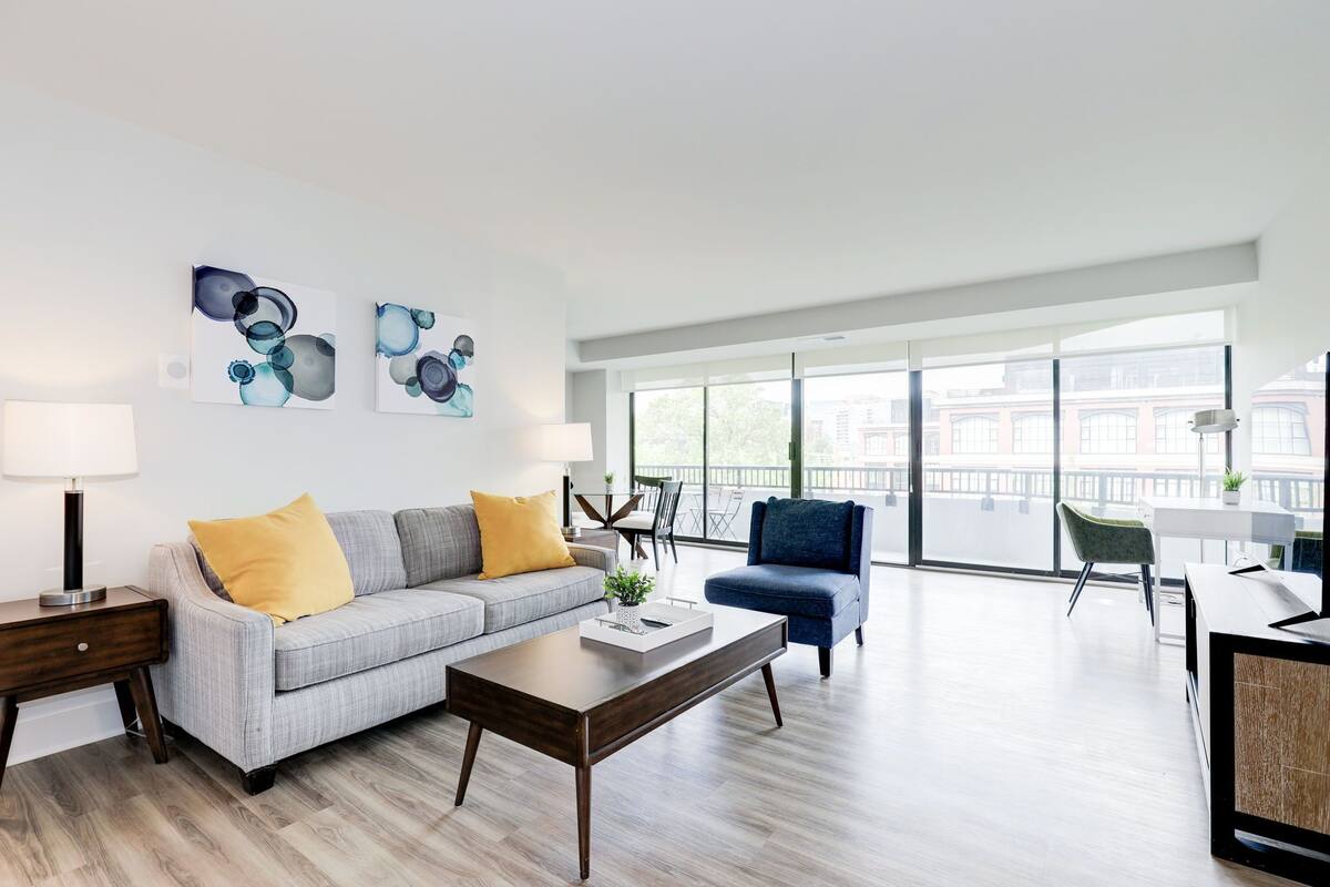 A modern living room with a grey sofa, a blue armchair, a wooden coffee table, and artwork on the wall.