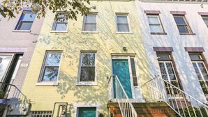 A row of three-story townhouses with a green door, white railings, and a brick facade. - Four Bedroom House Near Sports & Museums (Washington)