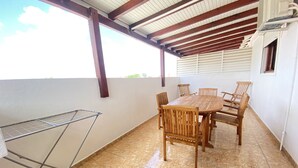 Un portico coperto con un tavolo e sedie di legno, una stendibiancheria in metallo e un pavimento piastrellato.