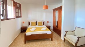 Un'ampia camera da letto con un letto grande, un armadio in legno, una sedia e una finestra con tende.