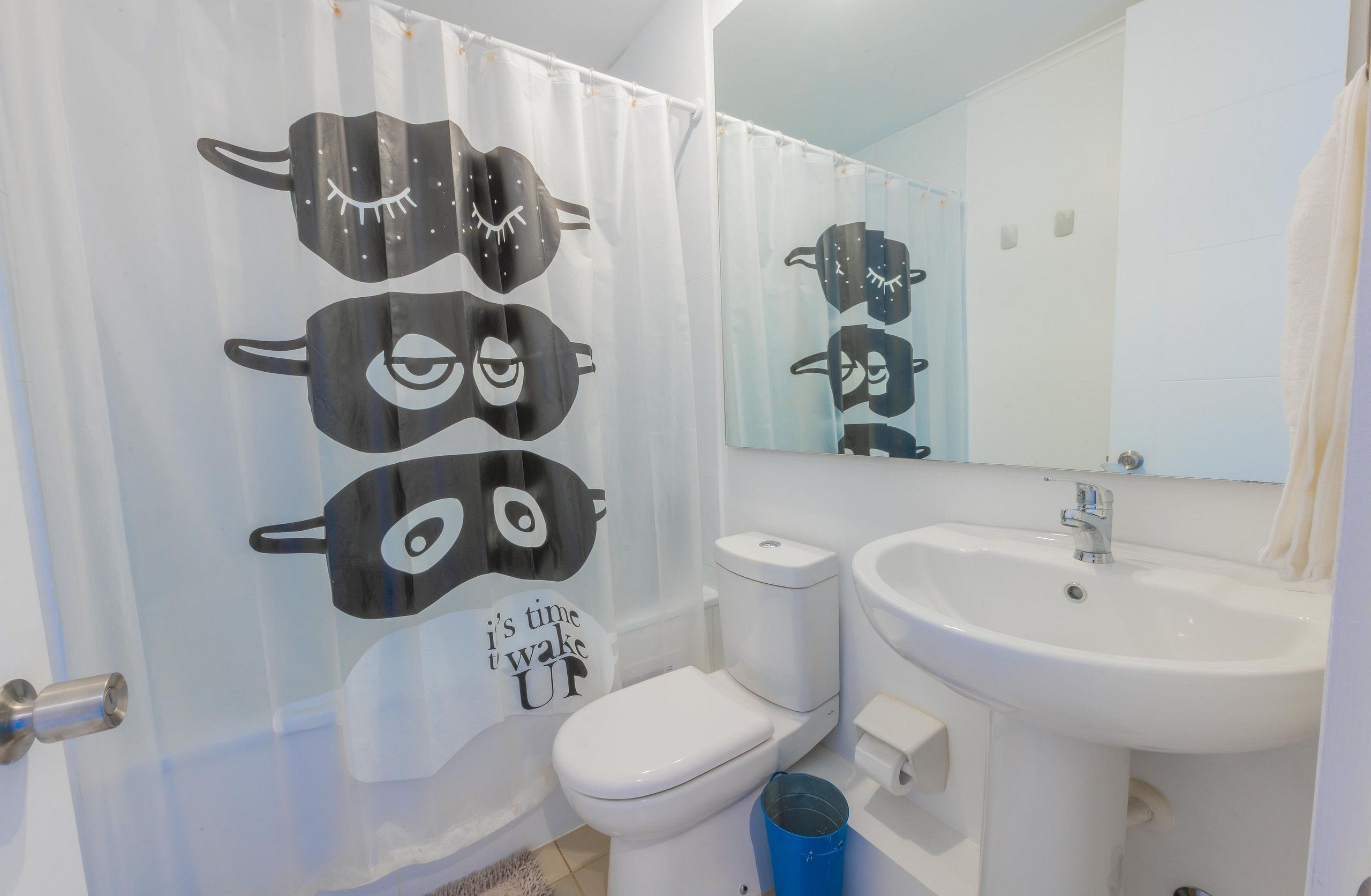A bathroom with a toilet, sink, and a shower curtain with a face design.