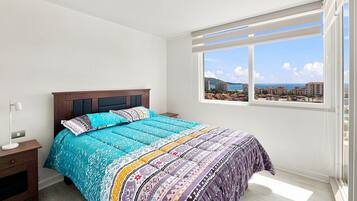 A bedroom with a large bed, a nightstand, a window with a view of buildings, and a ceiling light.