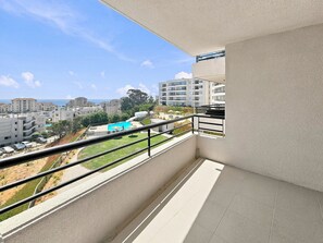 Ein Balkon mit Blick auf einen Swimmingpool, angrenzende Gebäude und einen klaren Himmel.