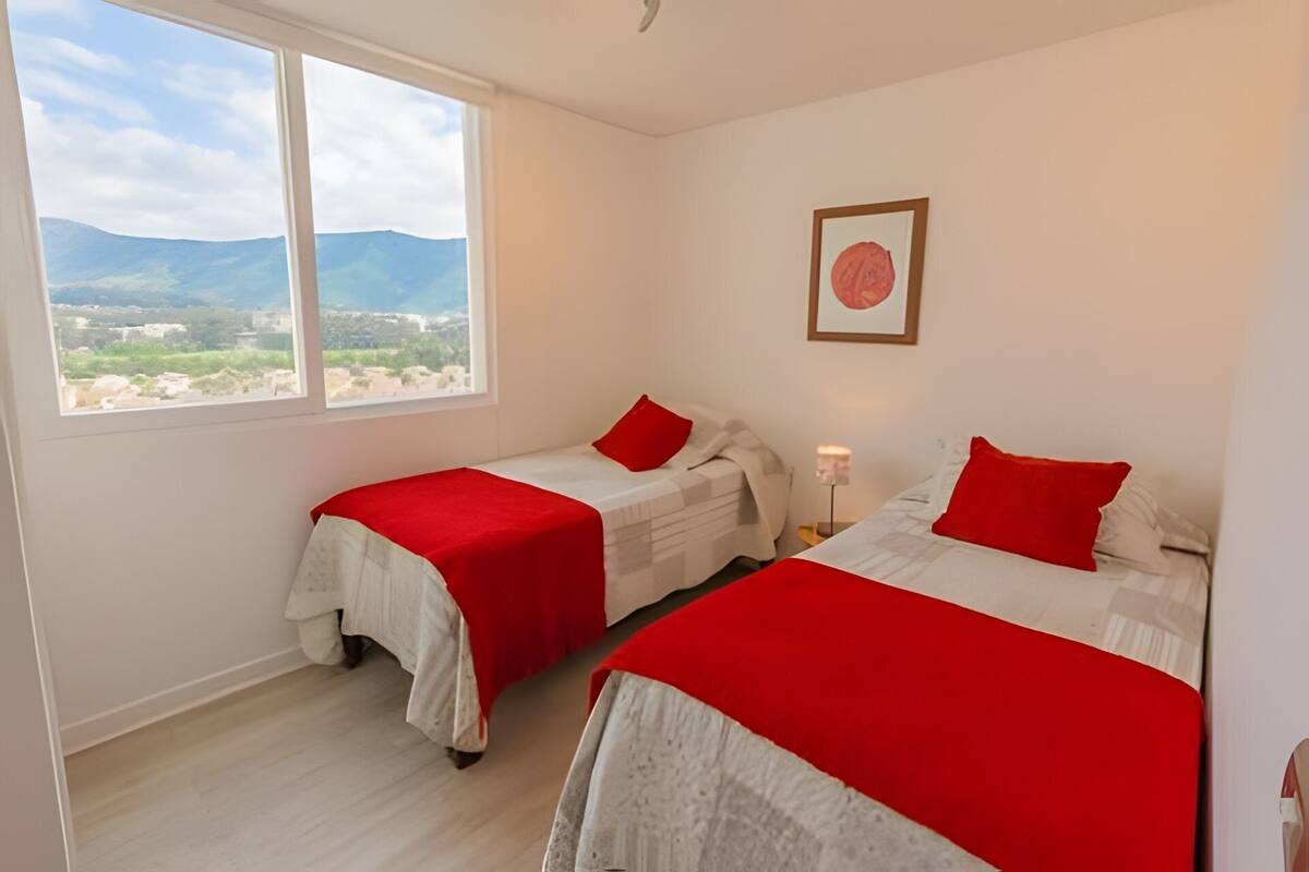 Una habitación con dos camas, una ventana con vistas a montañas y un cuadro en la pared.