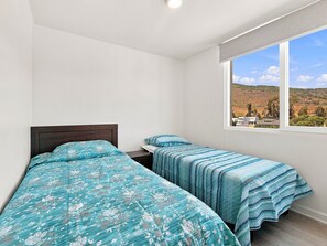 A bedroom with two beds, a window with a view of a hilly landscape, and a white ceiling.
