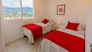 Una habitació amb dos llits, una finestra amb vistes a les muntanyes i un quadre al mur.