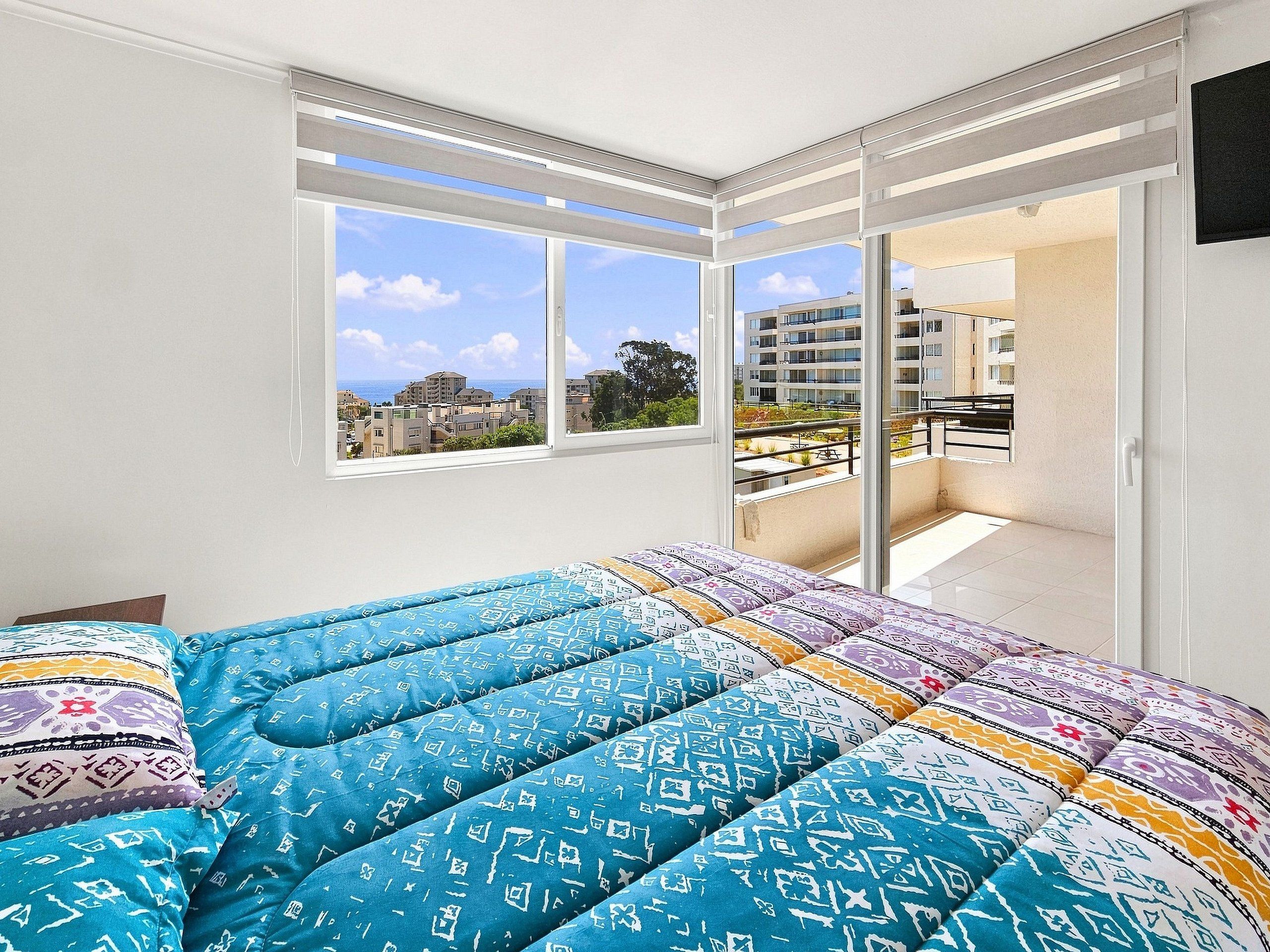 A bedroom with a bed, a window, and a view of buildings.