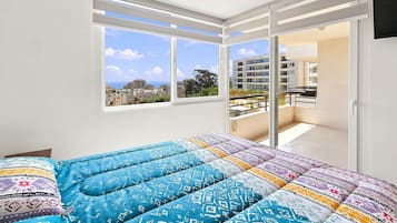 A bedroom with a bed, a window, and a view of buildings.