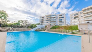 A swimming pool with a water slide, surrounded by a fence, and adjacent to a multi-story building. - Oceana Suites Papudo (Papudo)