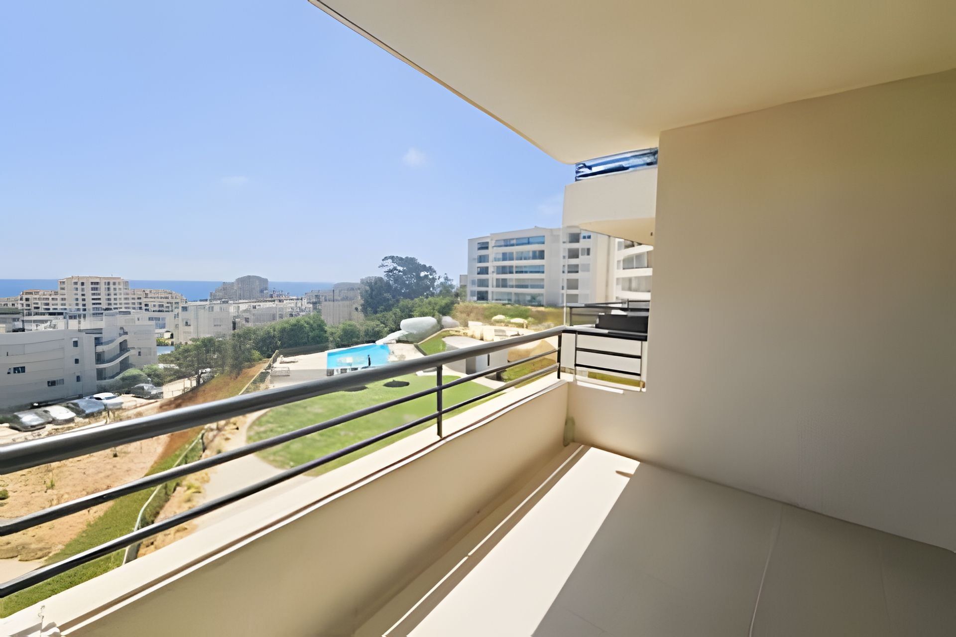 A balcony with a metal railing, a view of a cityscape, and a clear sky.