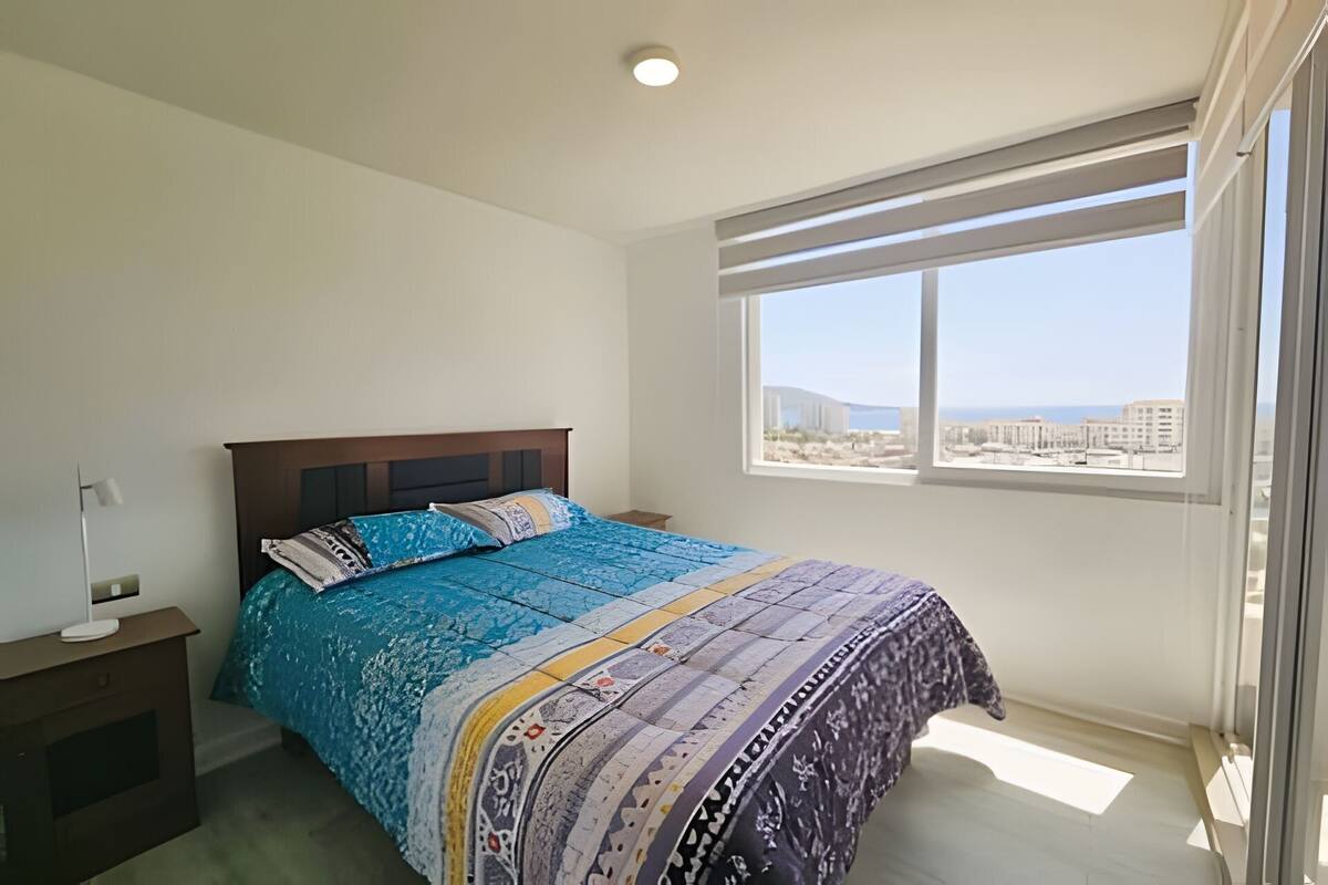Un dormitorio con cama, mesita de noche, ventana con vistas y luz en el techo.